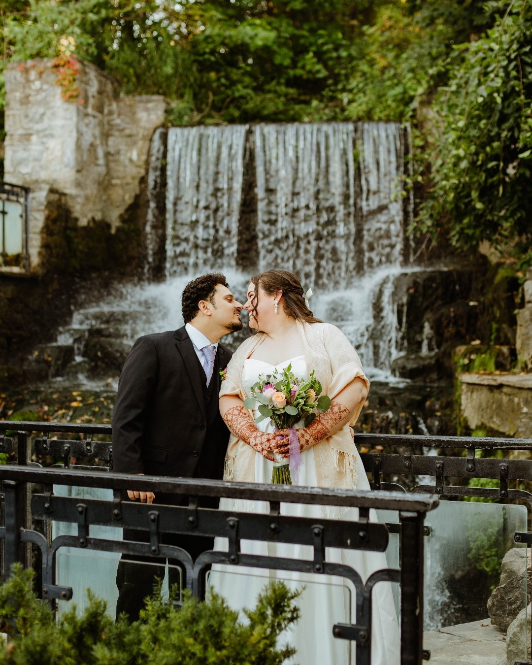 Bride and groom nose to nose in front of the waterfall at Ancaster Mill.
