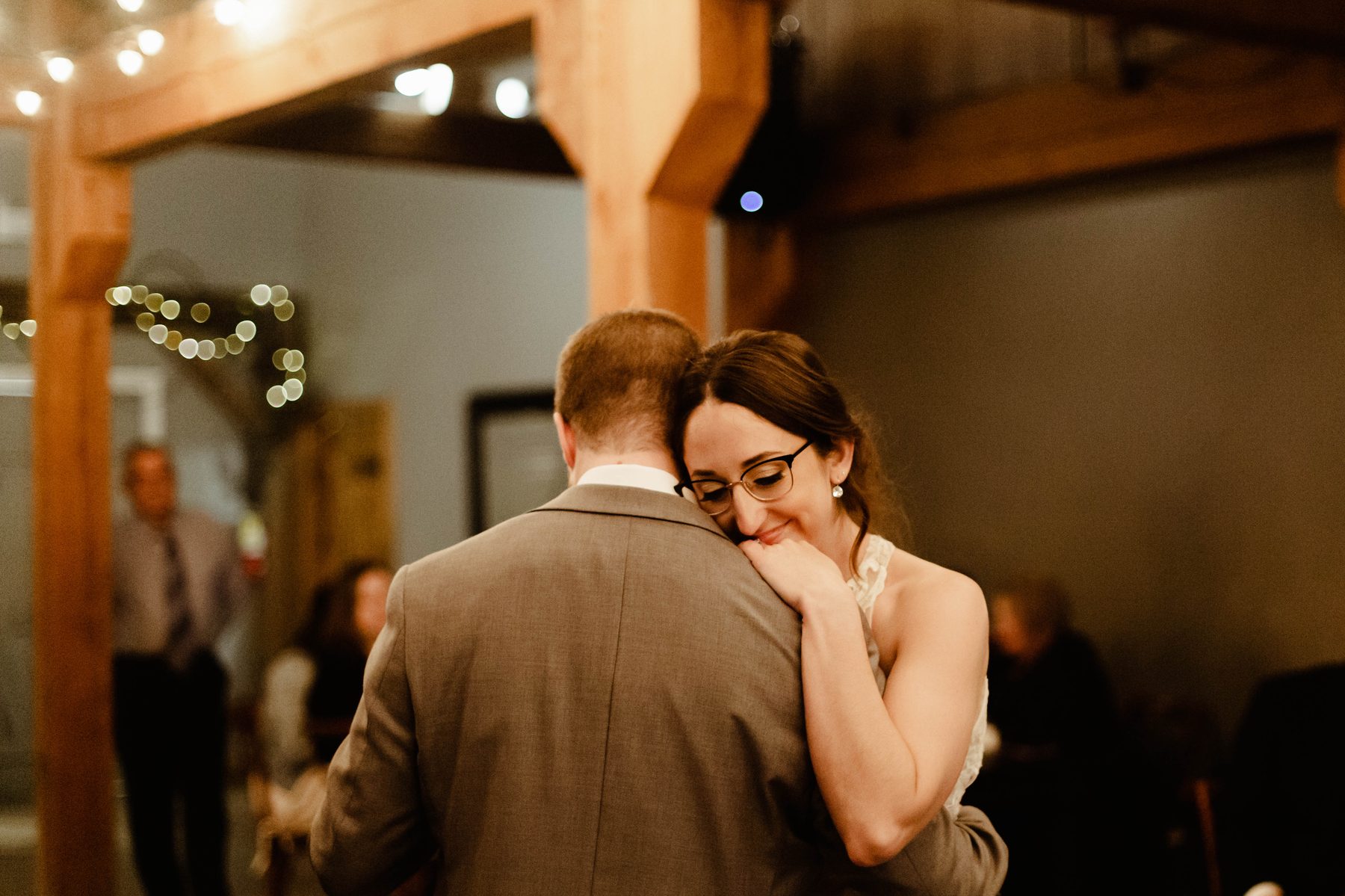 Couple slow dancing cheek to cheek under string lights at their reception.
