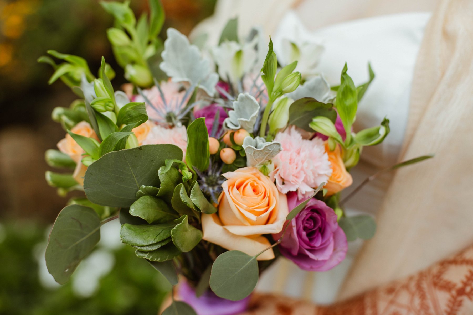 Close-up detail of a bouquet with orange and purple roses, carnations, and eucalyptus.