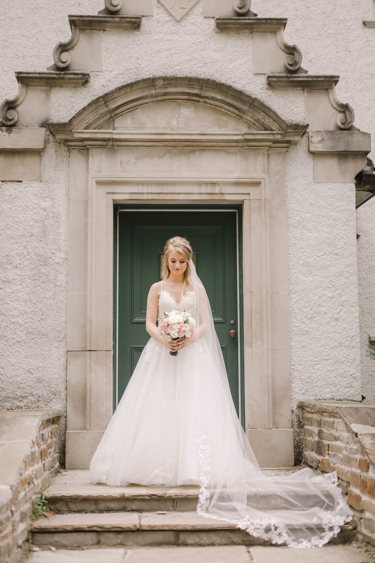 Bride standing in a stone archway in front of a green door, holding her bouquet.