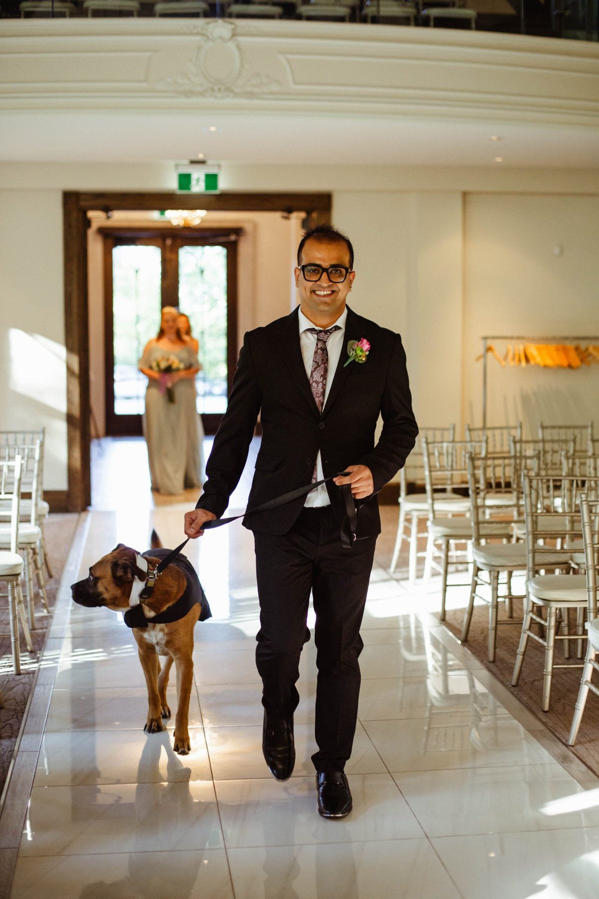 Groom smiling as he walks the couple's dog, dressed in a tuxedo, down the aisle.