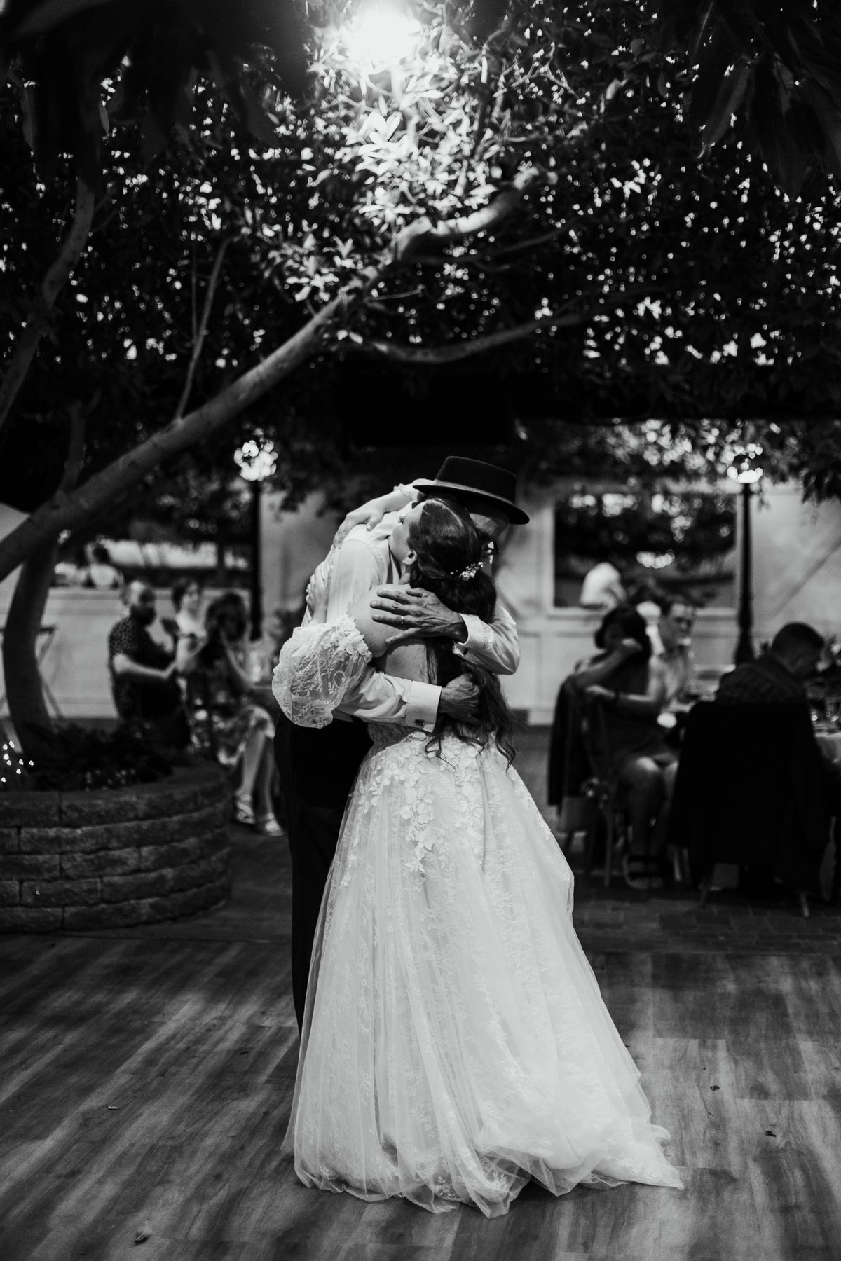 Black and white photo of a bride slow dancing with her father under string lights.