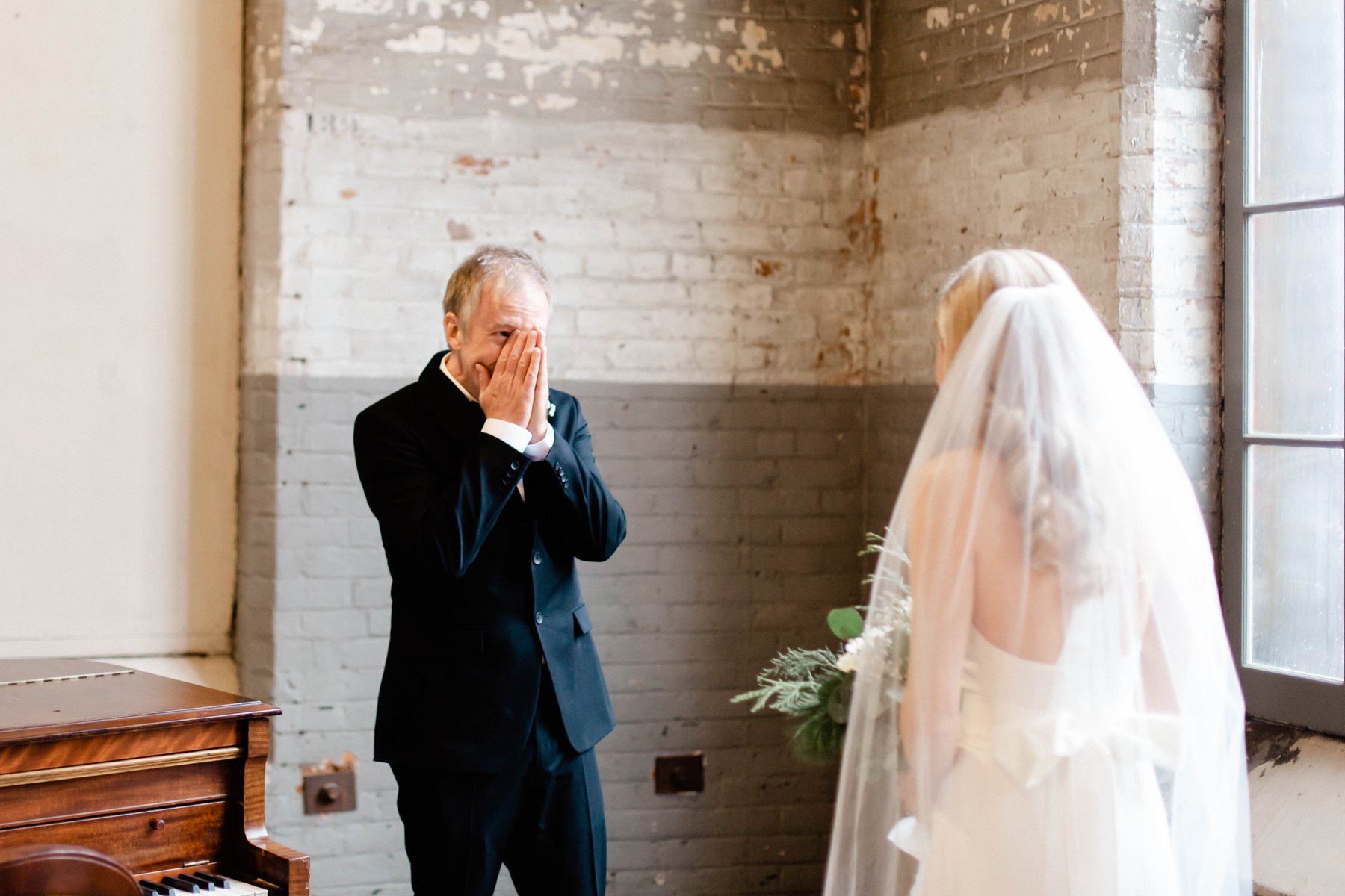 A father covering his face with his hands, overcome with emotion, seeing his daughter in her wedding dress for the first time.
