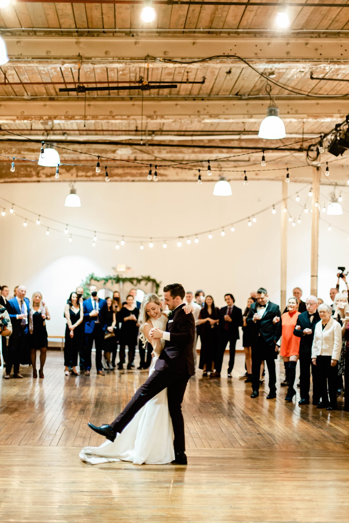 Bride and groom sharing their first dance in an industrial loft venue as guests watch.