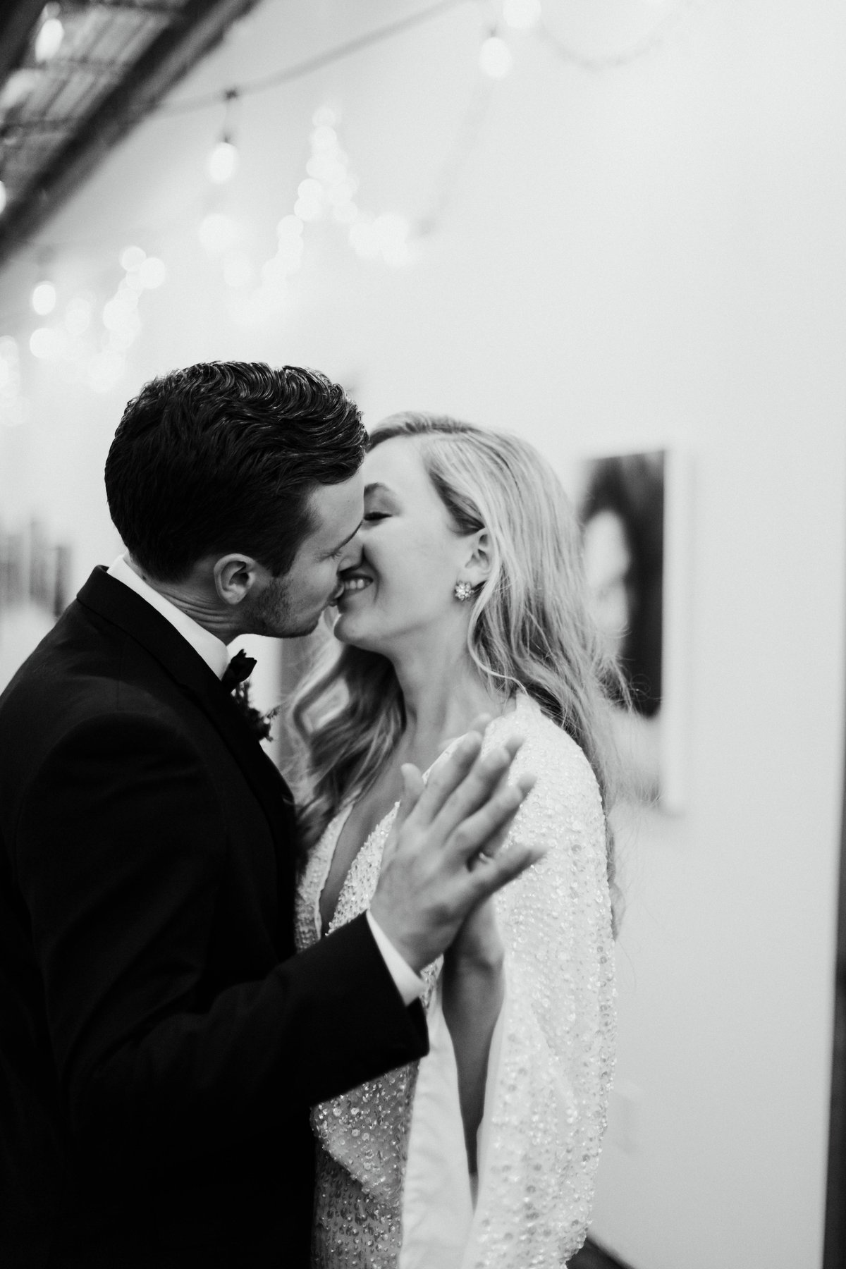 Black and white close-up of a bride and groom about to kiss in a gallery-style venue.