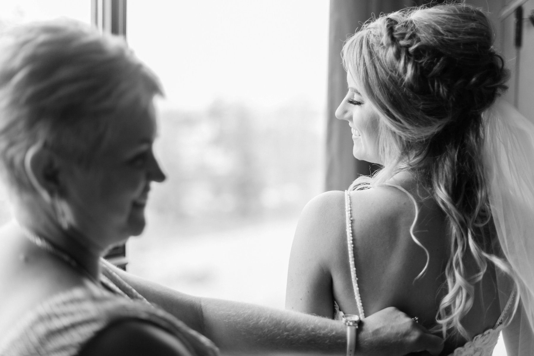Black and white photo of a mother fastening her daughter's necklace while getting ready.