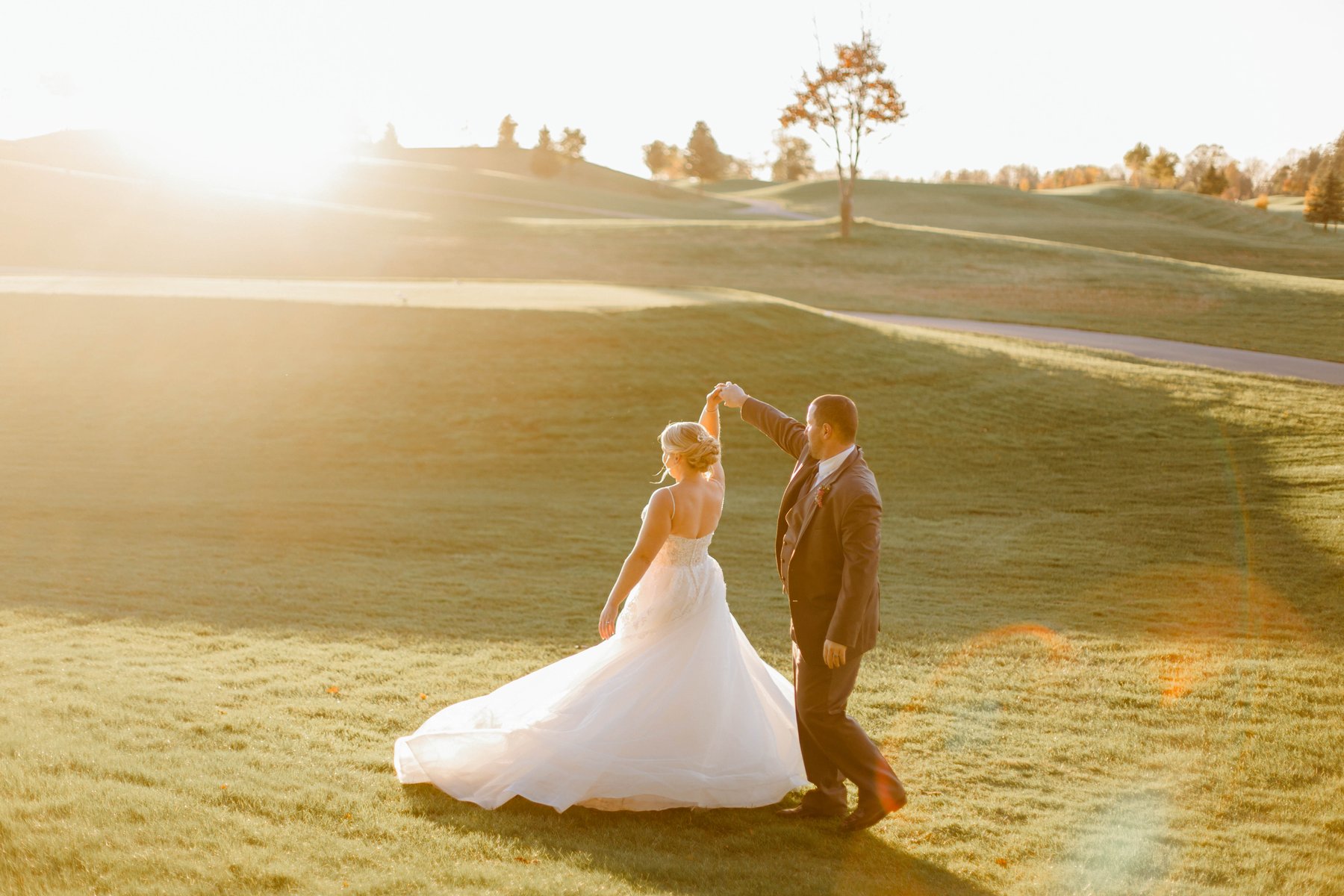 Bride and groom dancing together on a golf course at golden sunset.