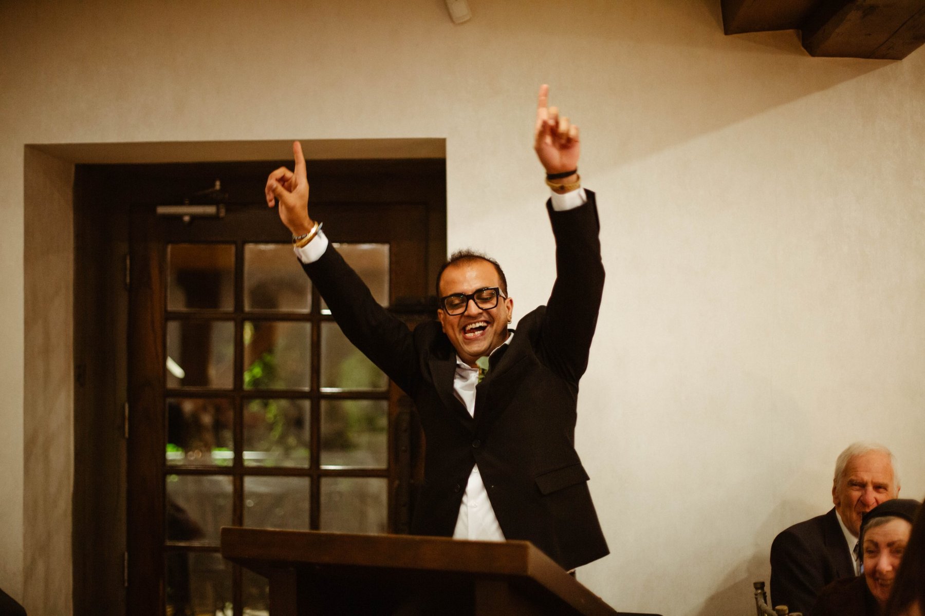 Groom cheering with both arms raised during a reception toast.