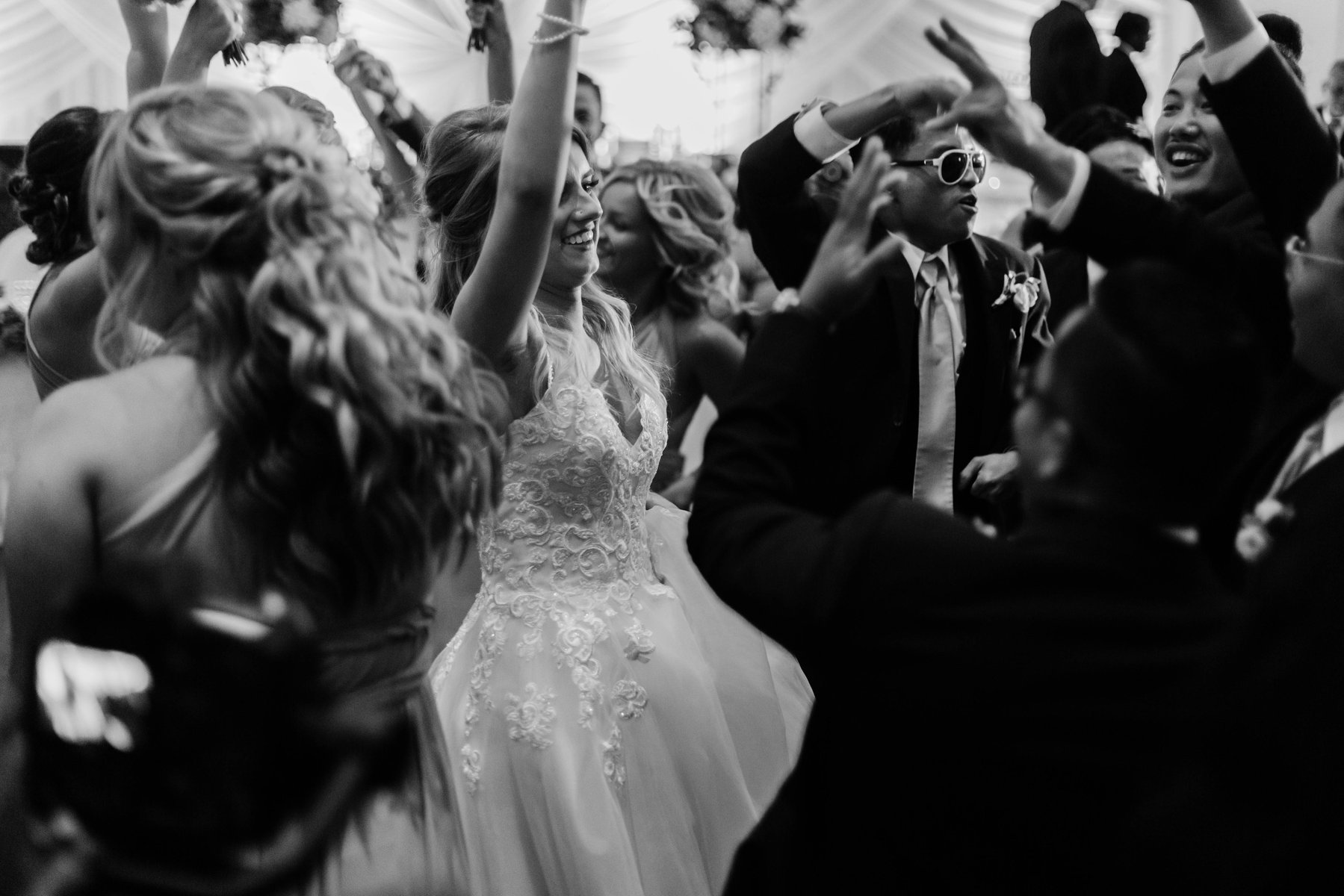 Black and white photo of a bride and guests dancing with hands raised.