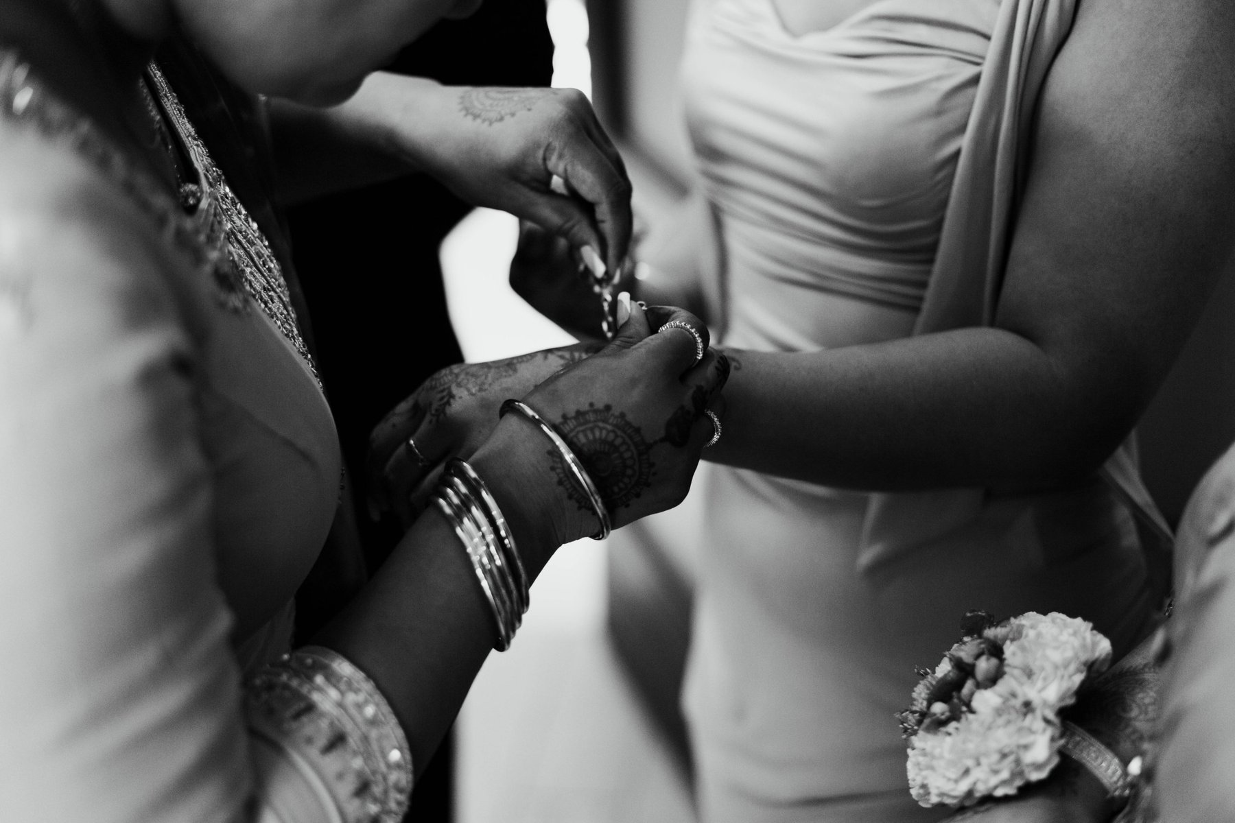 Black and white close-up of two henna-painted hands fastening a bracelet before the ceremony.