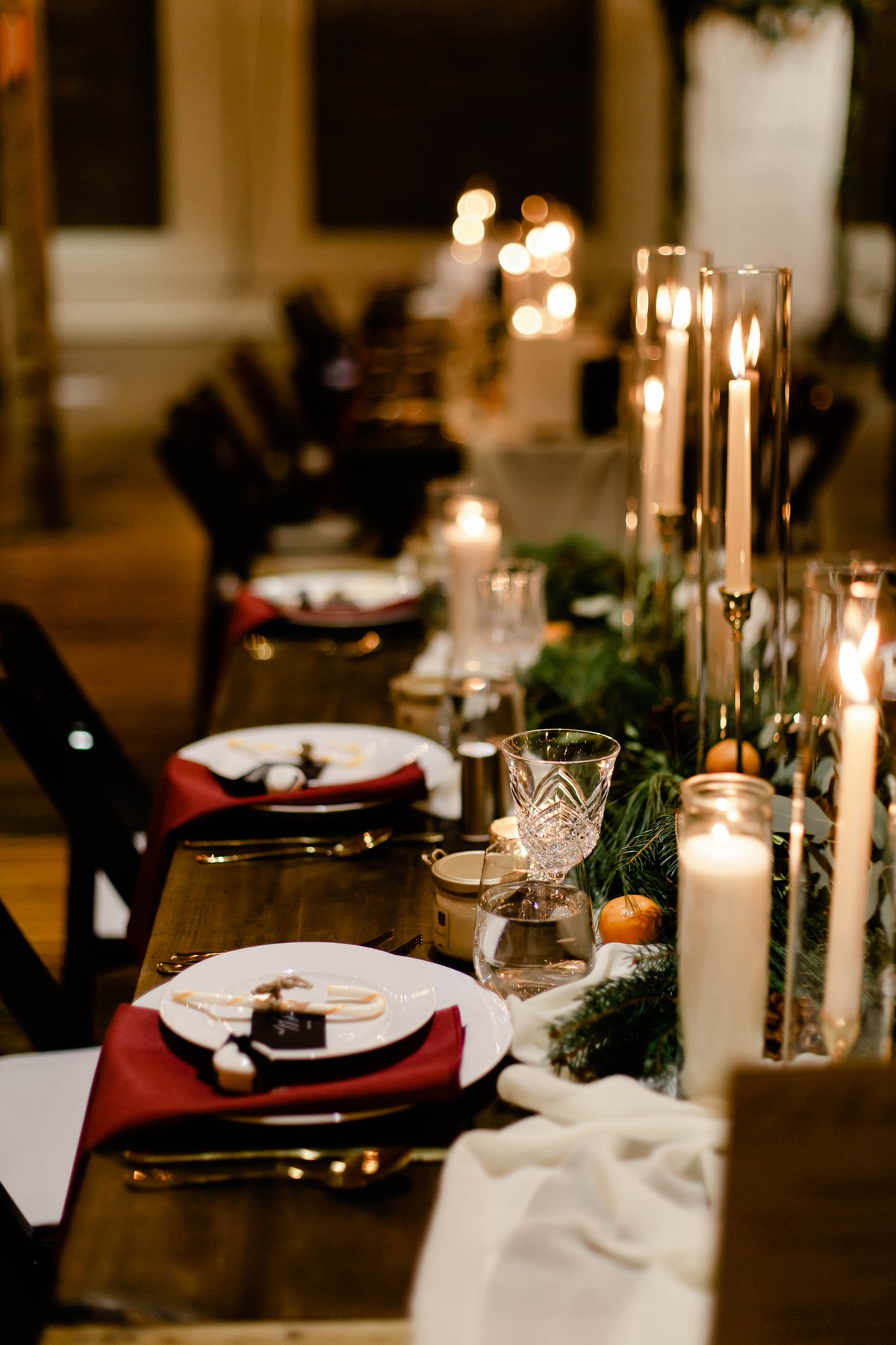 A candlelit holiday reception table setting with greenery, oranges, and candy canes.
