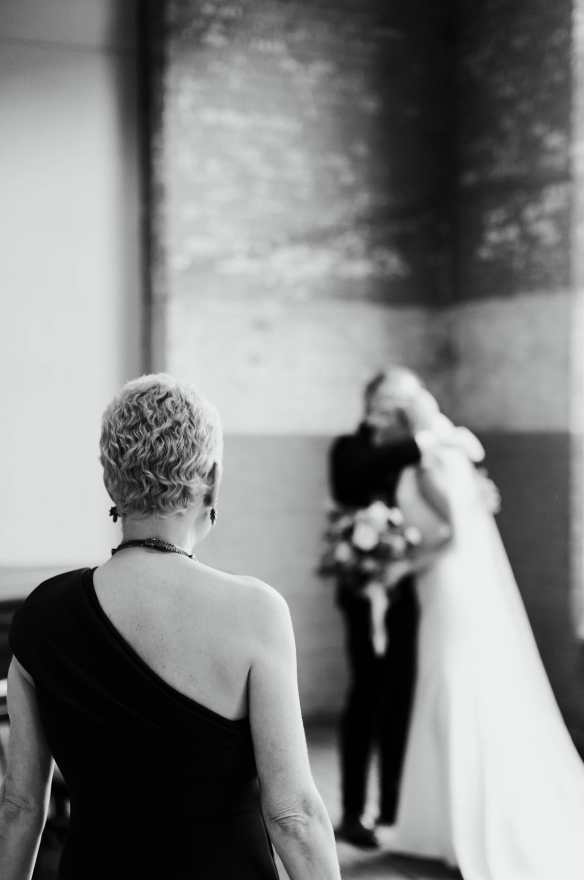 Black and white photo of a mother watching her son and his bride share a quiet moment.