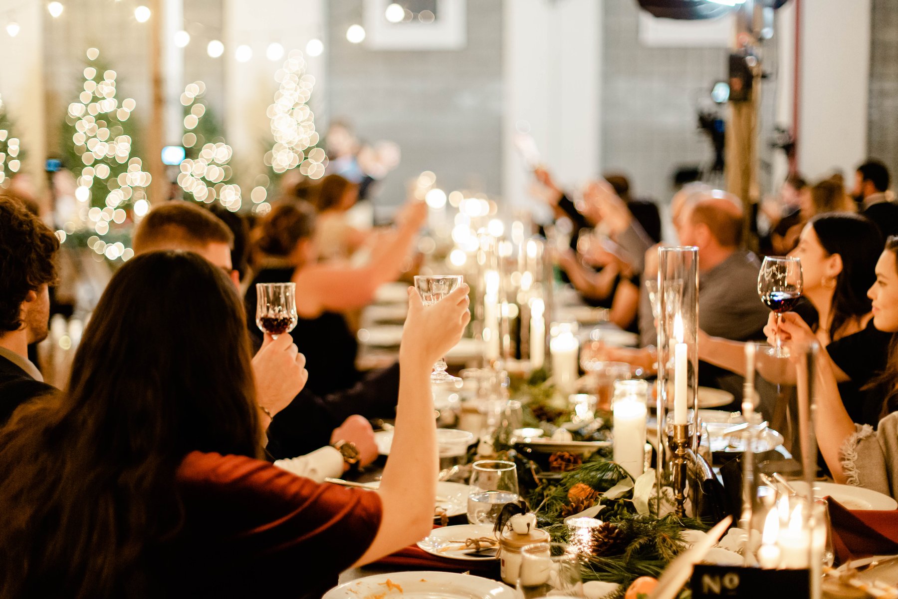 Wedding guests raising their glasses for a toast at a candlelit holiday reception table.