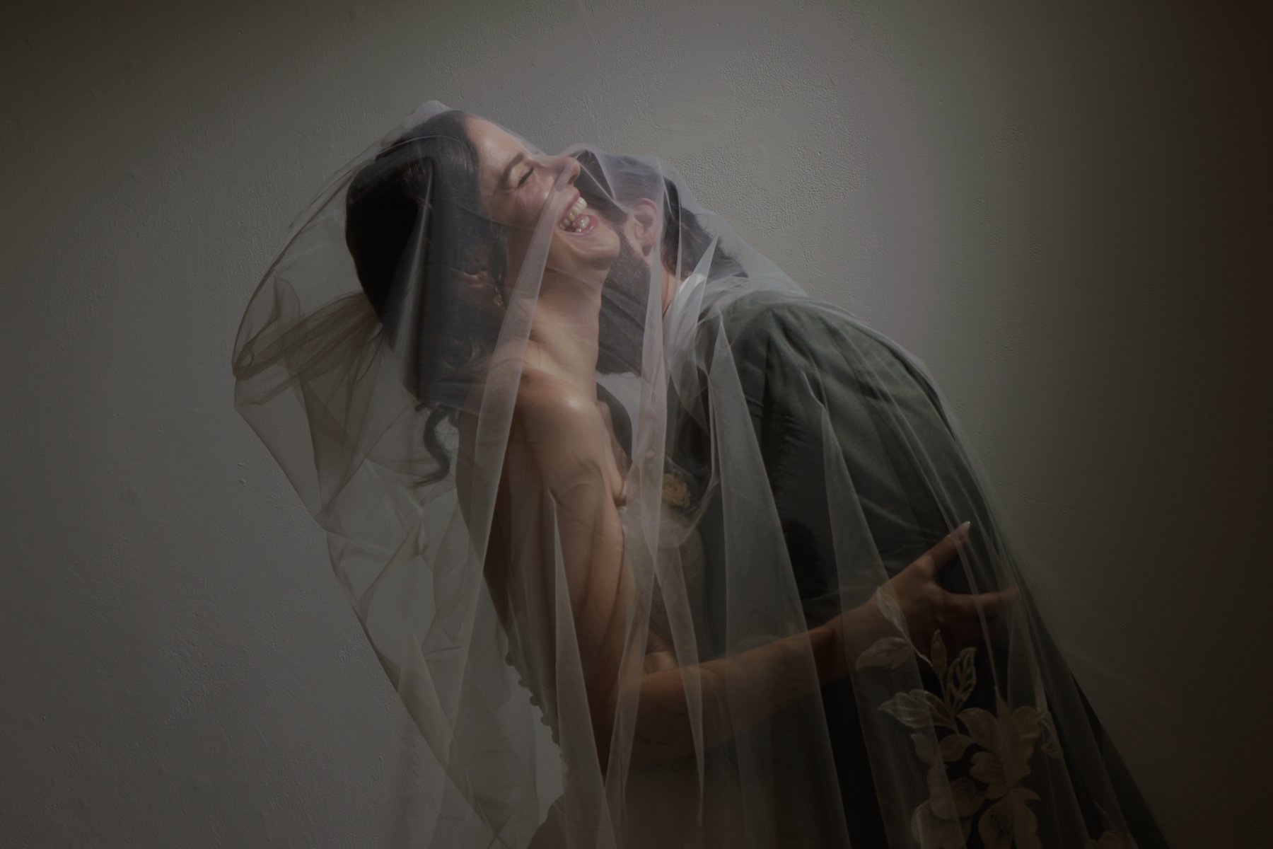 Motion-blurred double exposure of a bride and groom laughing together under her veil.