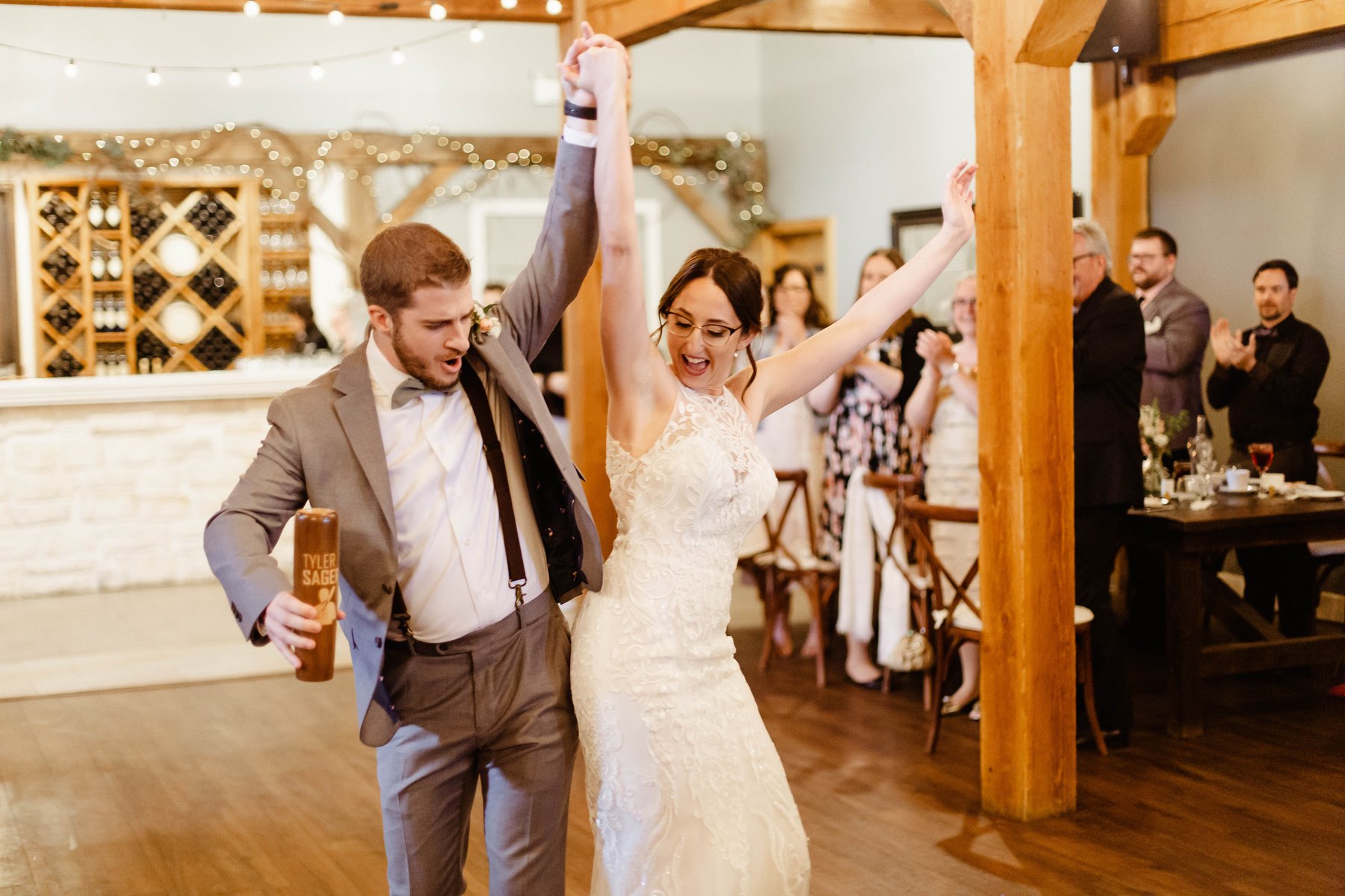 Bride and groom cheering with hands raised as they enter their winery reception.